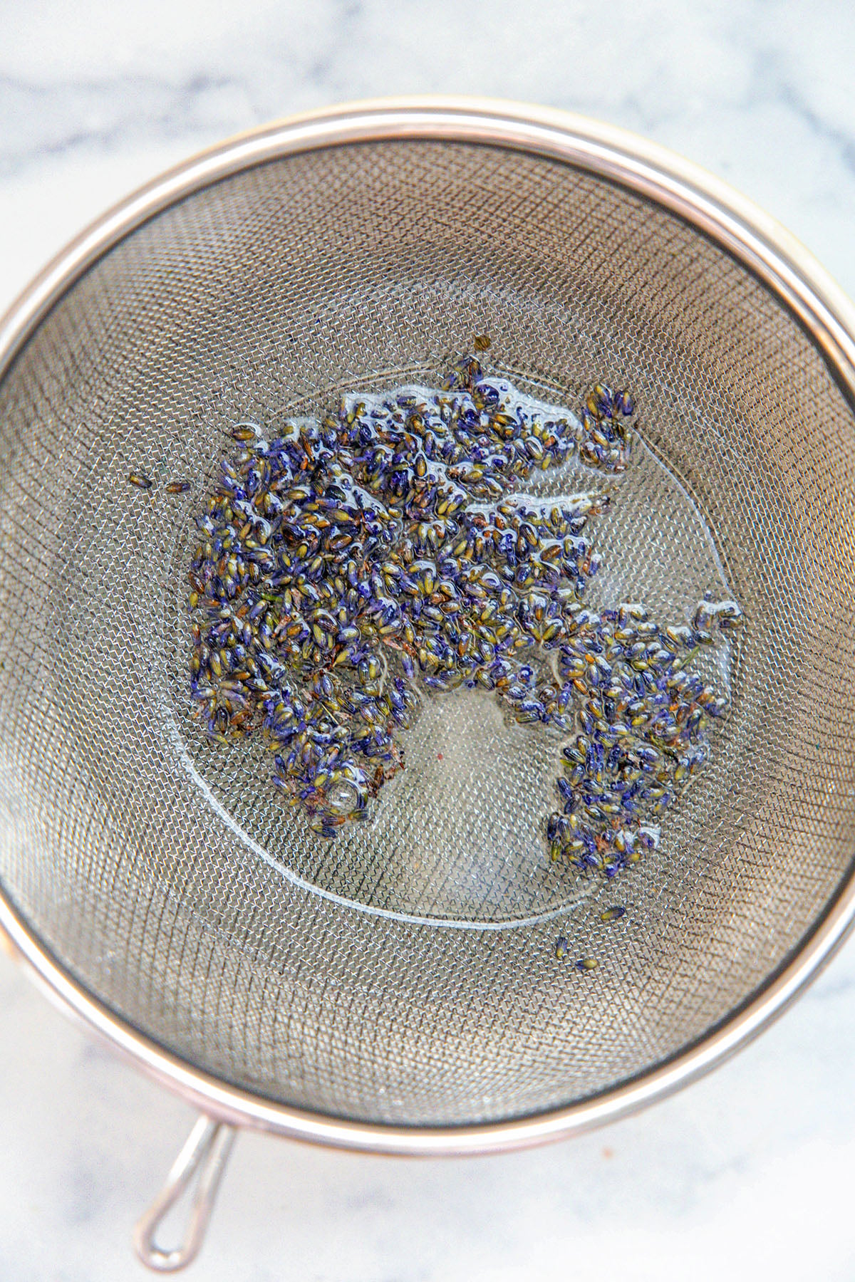 Overhead view of dried lavender being strained out of syrup into bowl.