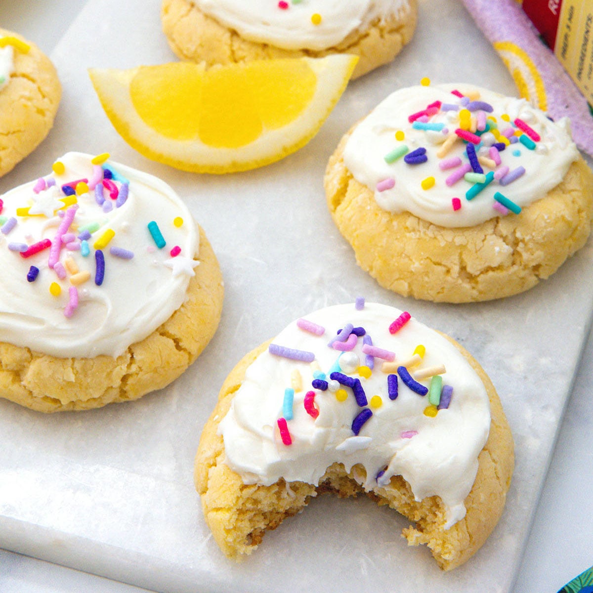 Closeup view of lemon cake mix cookie with bite taken out of it with more cookies in the background.