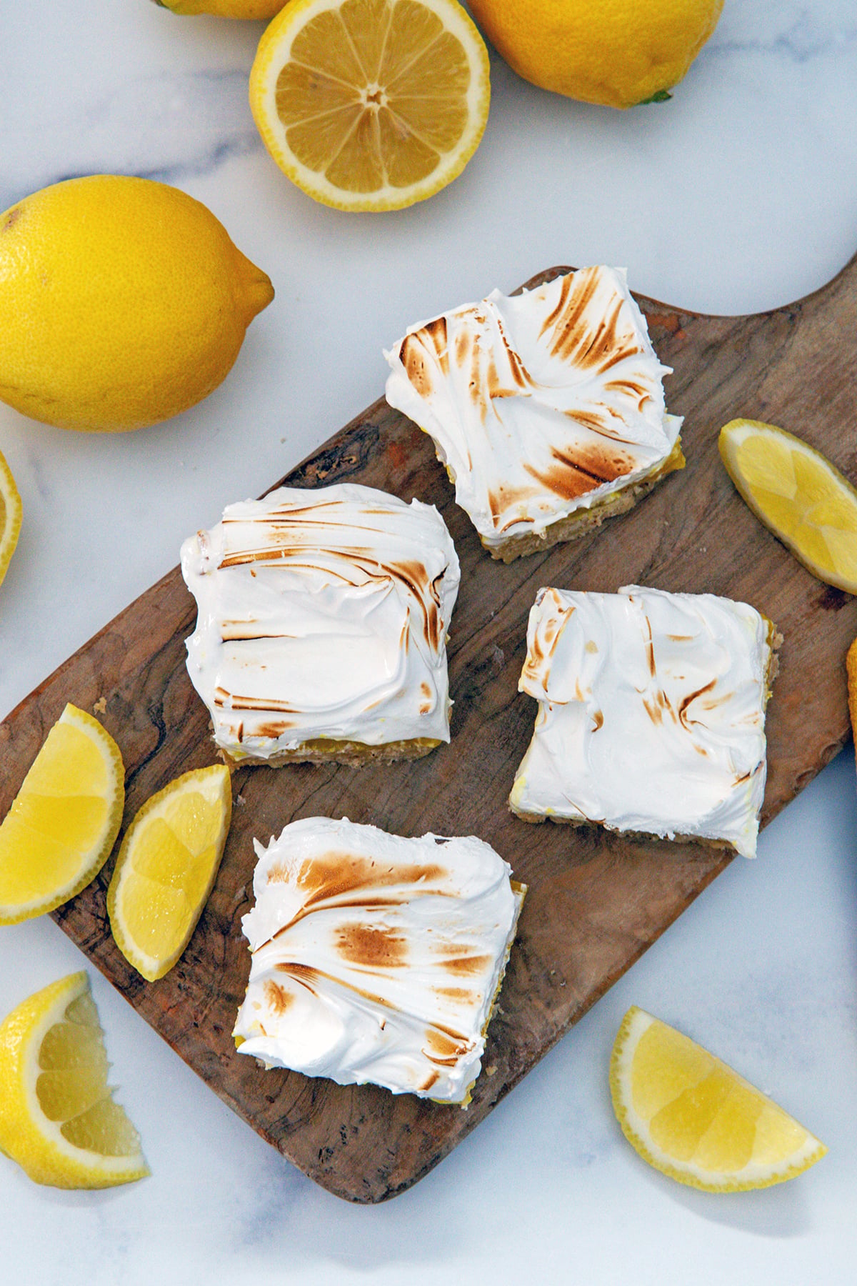 Overhead view of lemon meringue bars on wooden board to show toasted meringue topping with lemons all around.