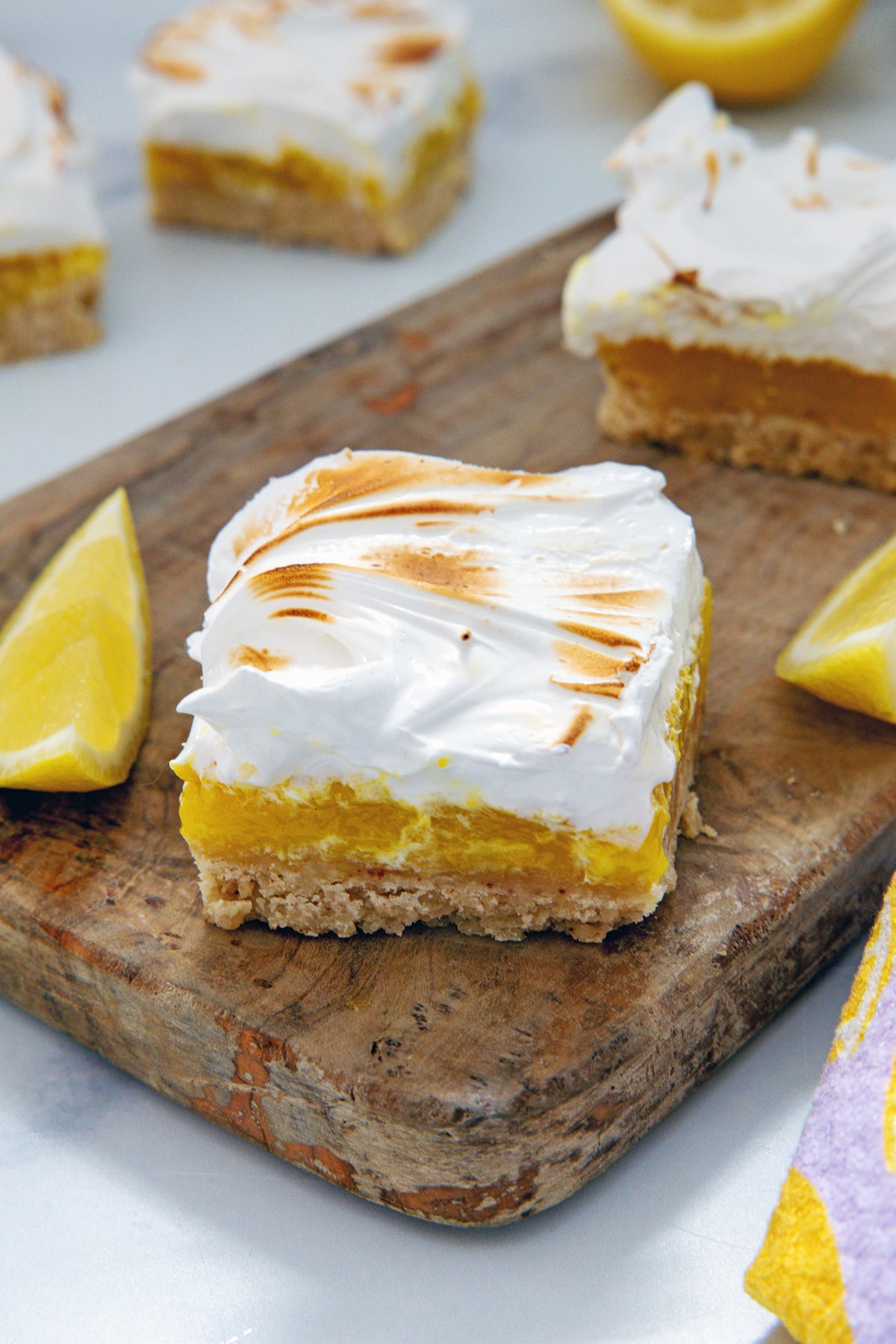 Lemon meringue bar on a wooden board with more bars and lemon slices in background.