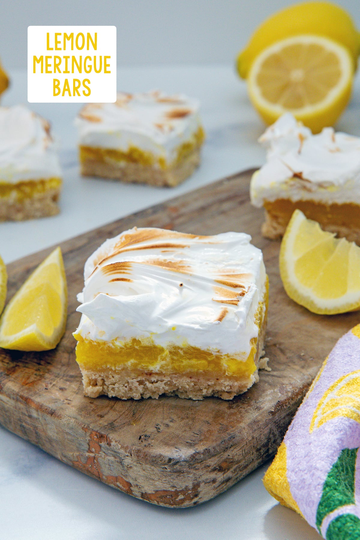 Lemon meringue bar on a wooden board with more bars and lemon slices in background and recipe title at top.