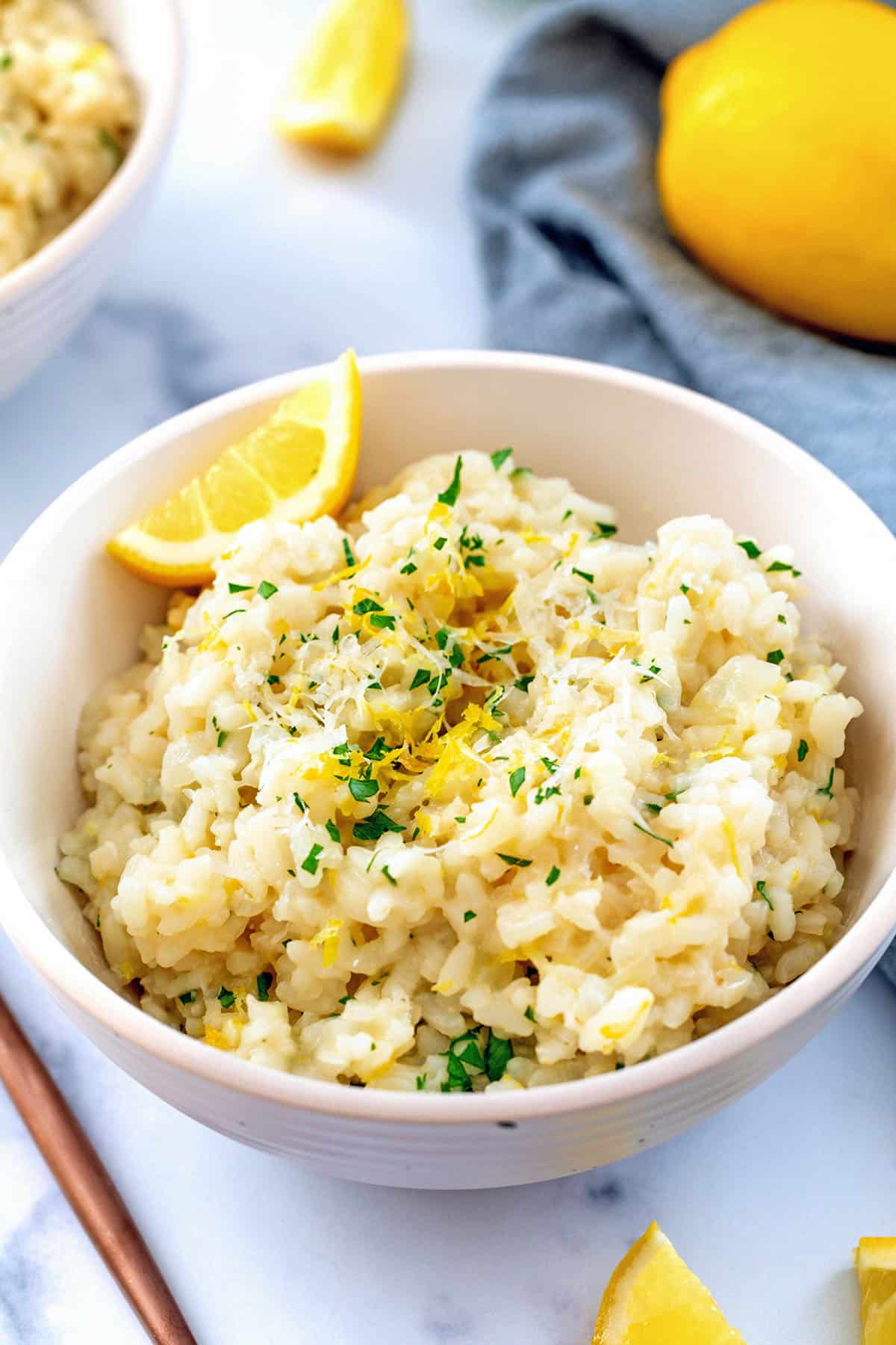 Overhead view of a bowl of lemon risotto with parsley and lemon wedges.