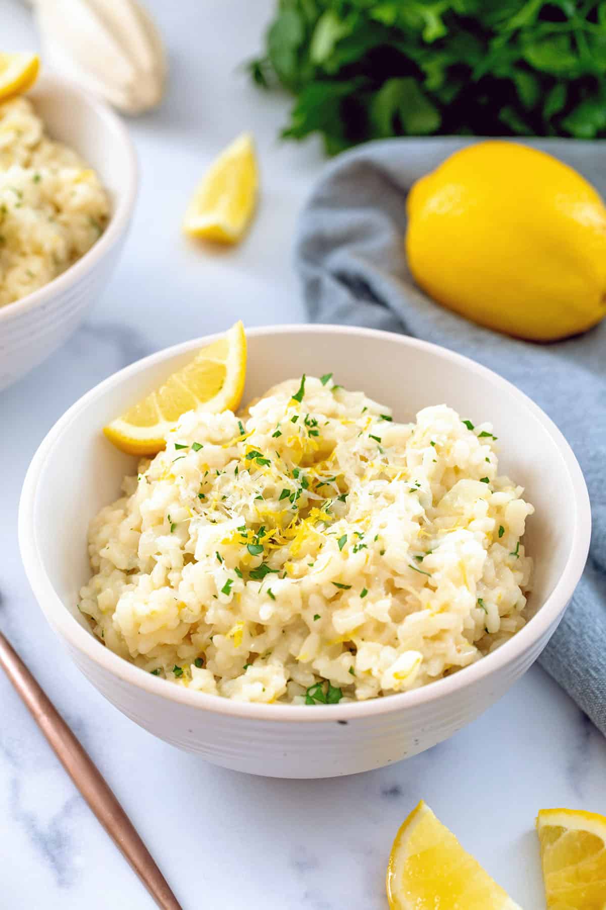 Bowl of lemon risotto with lemon wedges and bunch of parsley.