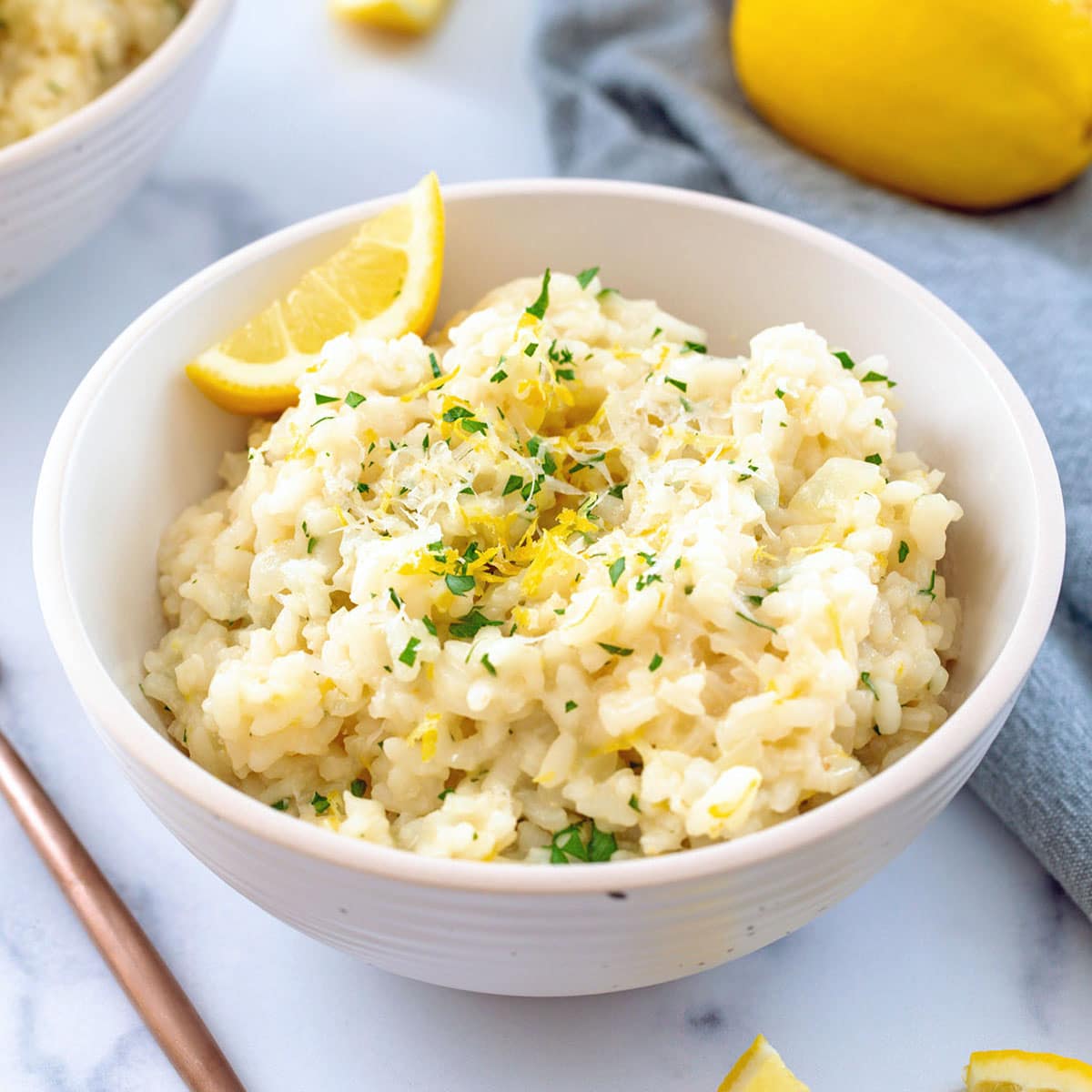 Closeup view of lemon risotto in a bowl with lemon wedge and parsley.