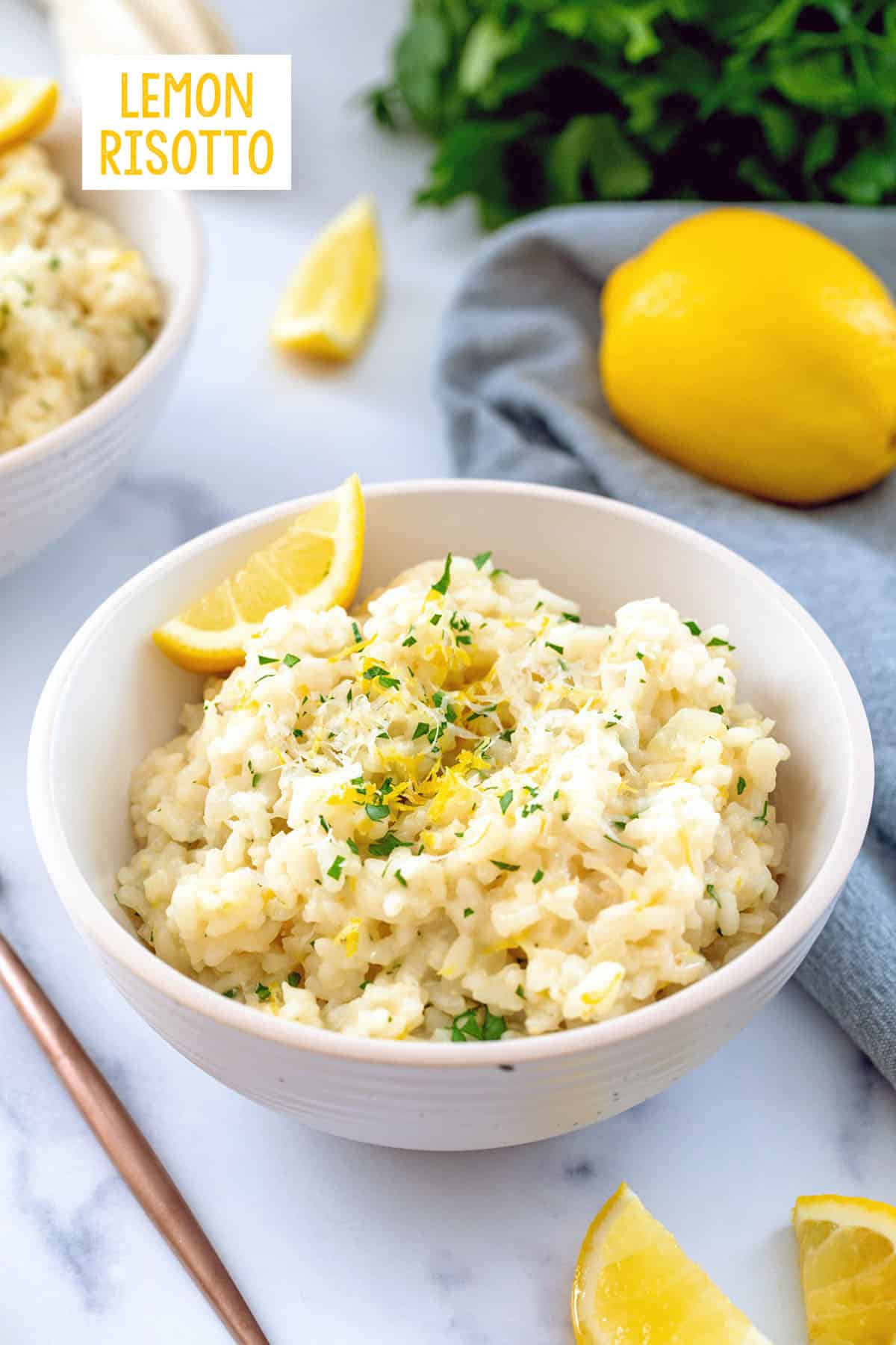 Bowl of lemon risotto with lemon wedges and bunch of parsley and recipe title at top.