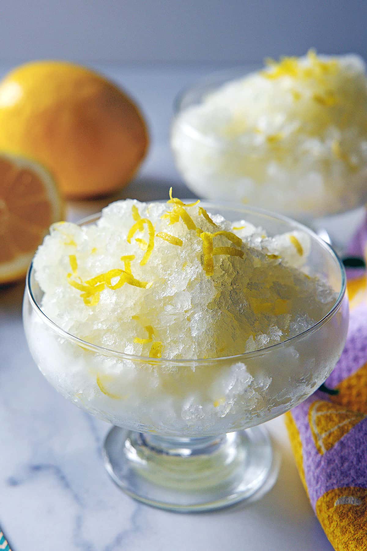 Head-on closeup view of a dish of lemonade granita with lemons in background.
