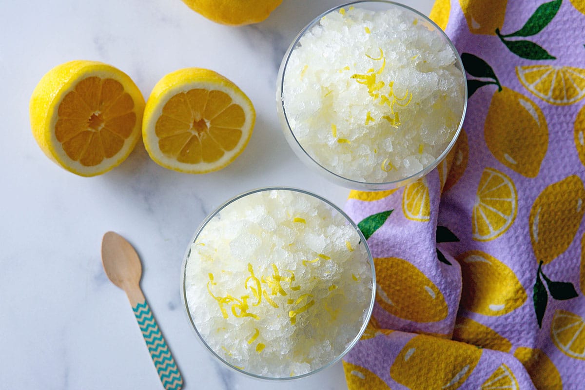 Overhead landscape view of two dishes of lemonade granita with lemon halves.