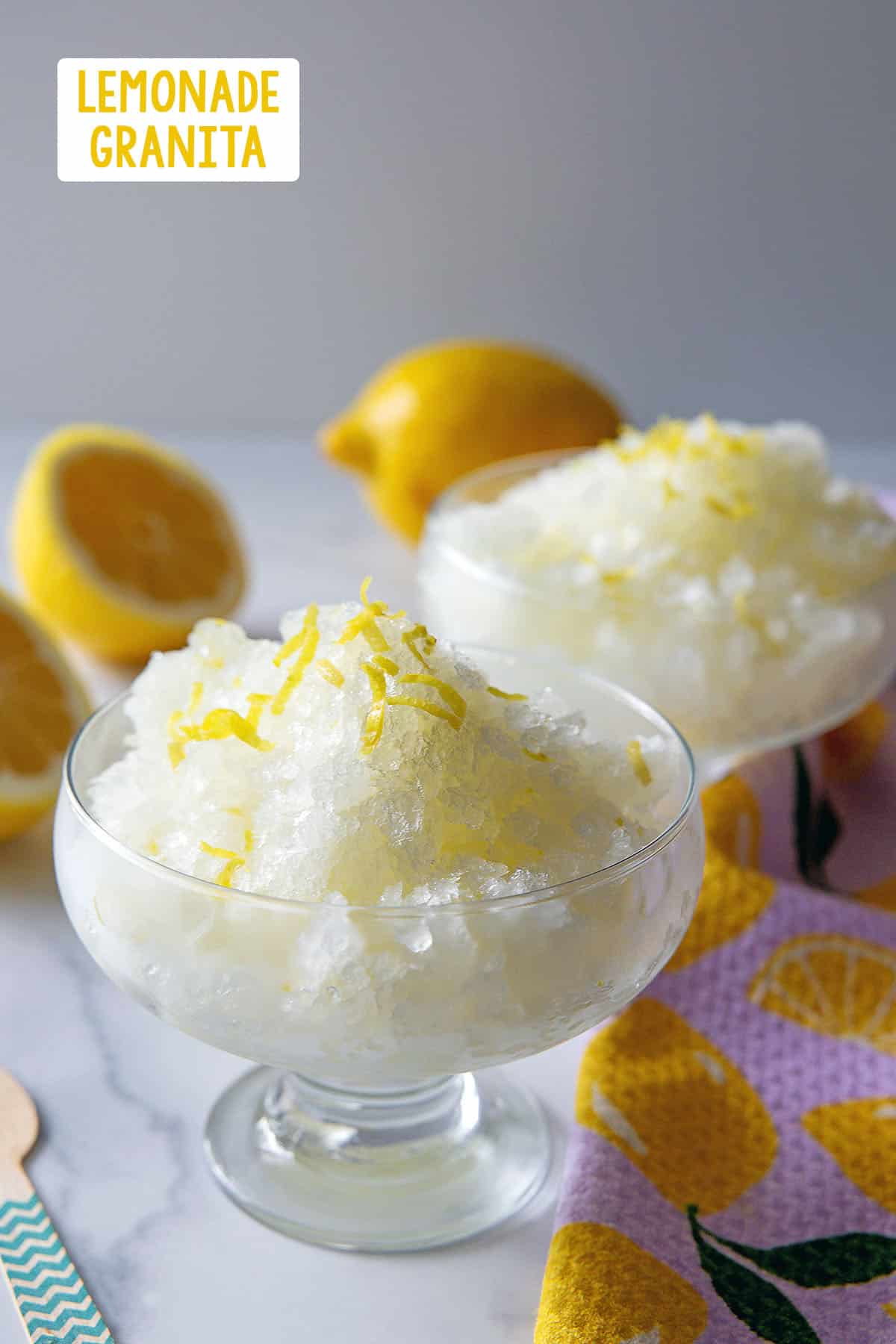 Two dishes of lemonade granita with lemon zest and fresh lemons in background with recipe title at top.