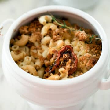 Closeup of bowl of macaroni and cheese with tomatoes and thyme sprig.