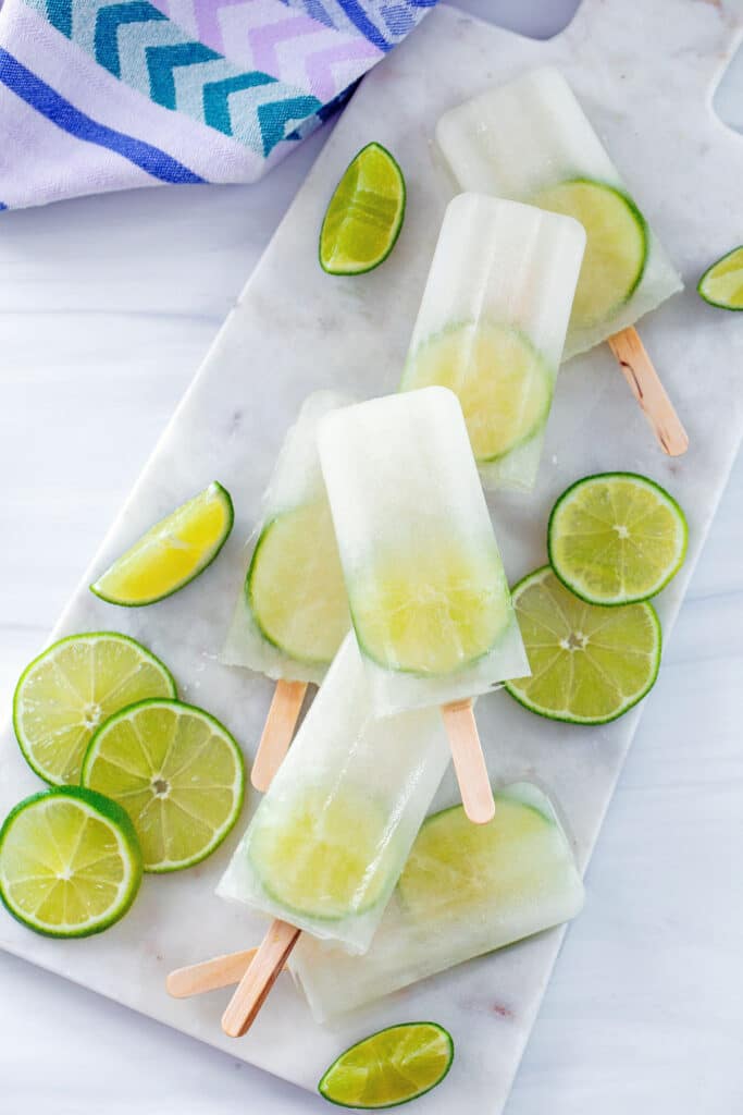Overhead view of six lime popsicles on a marble platter with lime slices all around.