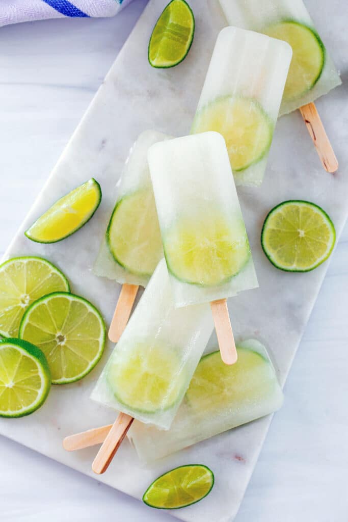 Overhead view of lime popsicles on a marble platter with sliced limes all around.