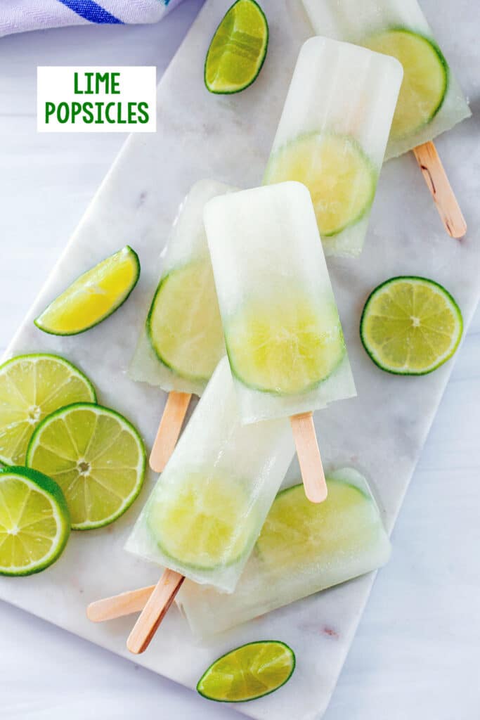 Overhead view of lime popsicles on a marble platter with sliced limes all around and recipe title at top.