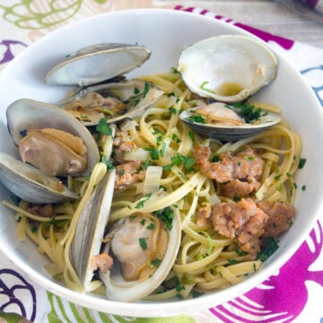 Closeup view of a white bowl of linguine with clams and sausage.