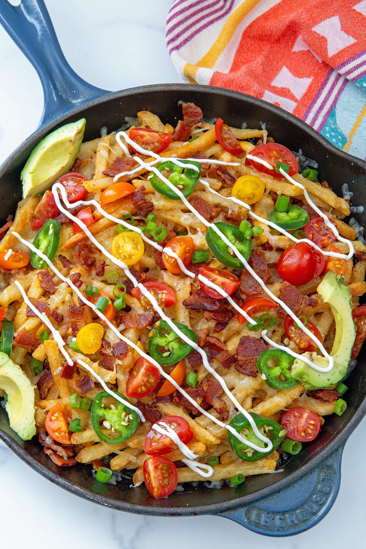 Cast skillet pan with french fries topped with cheese, bacon, tomatoes, jalapeños, scallions, avocado, and sour cream.