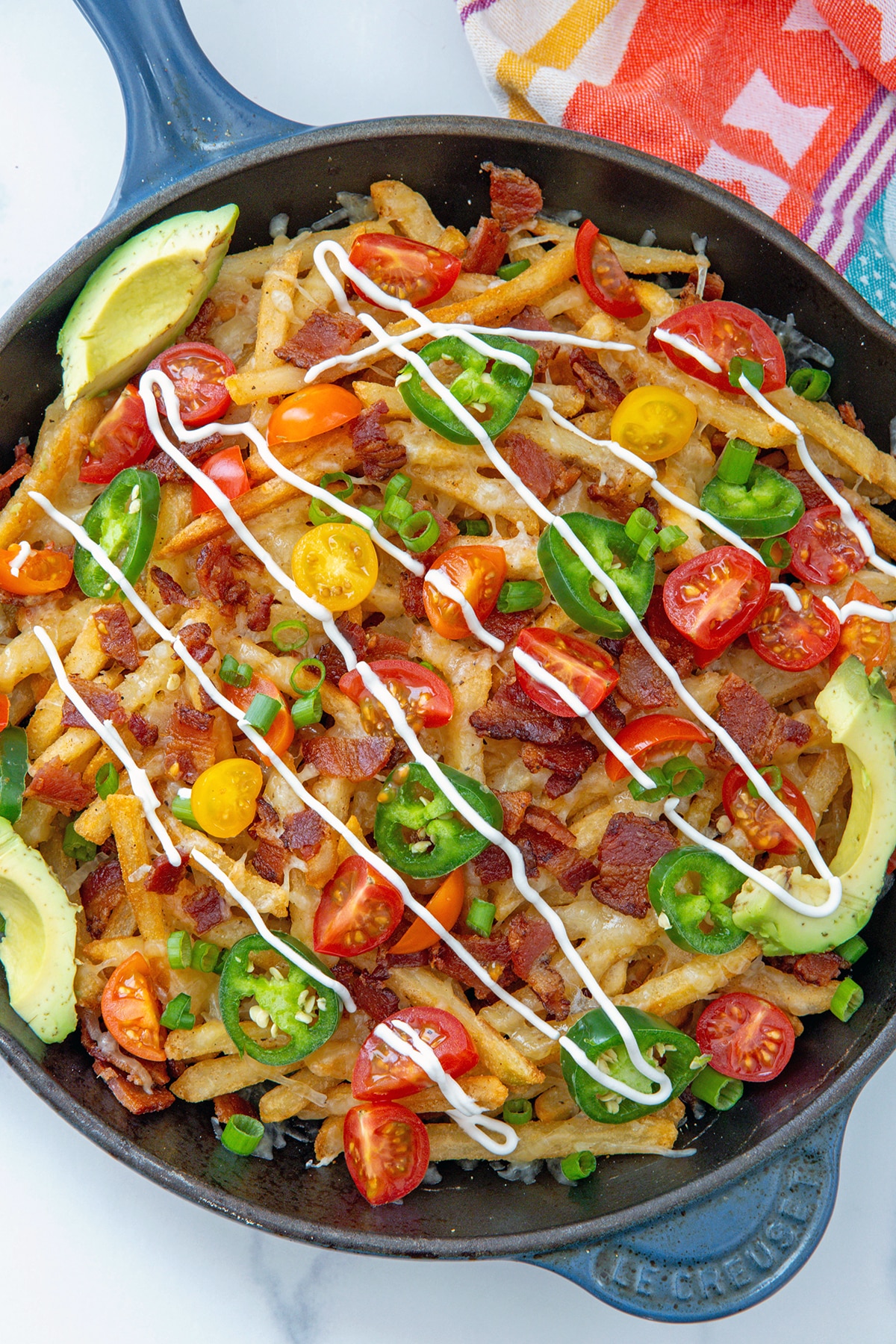 Overhead view of loaded fries with tomatoes, cheese, bacon, sour cream, jalapeños, and avocado.