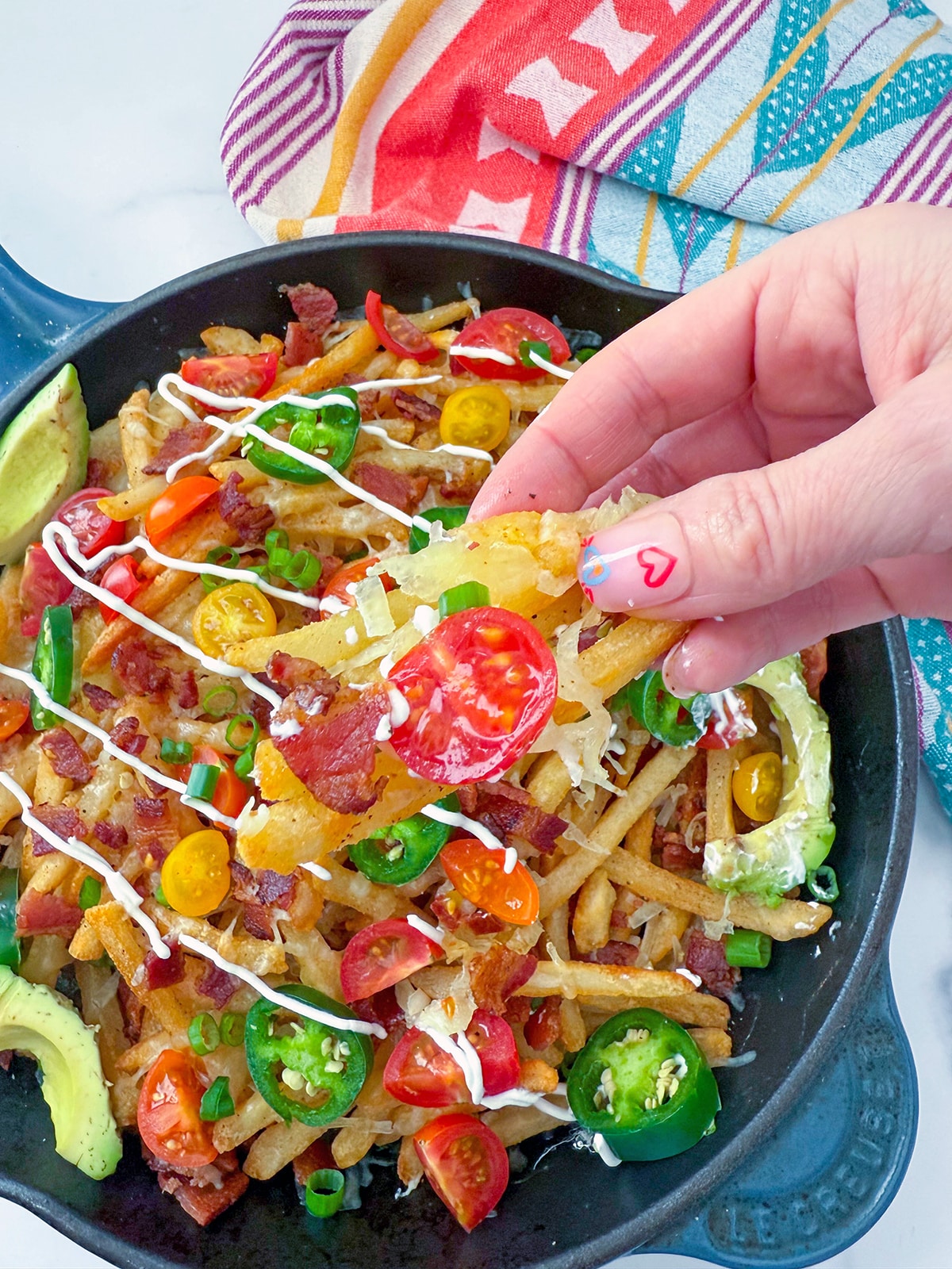 Hand picking up loaded fries in skillet.