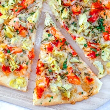 Closeup view of a lobster and artichoke flatbread pizza with a slice pulled out of it.