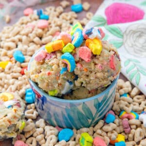 Close-up view of Lucky Charms cookie dough topped with marshmallows in a colorful bowl surrounded by cereal.