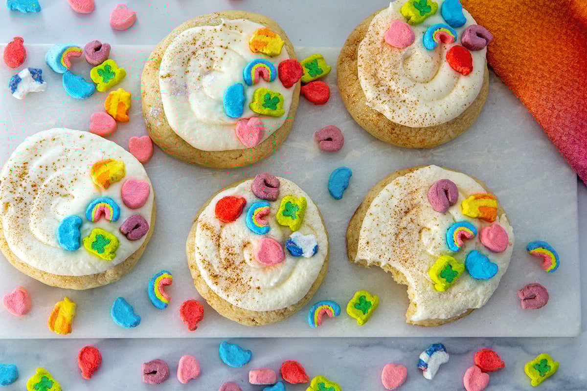 Landscape overhead view of multiple Lucky Charms cookies with frosting on a marble platter with cereal marshmallows all around.