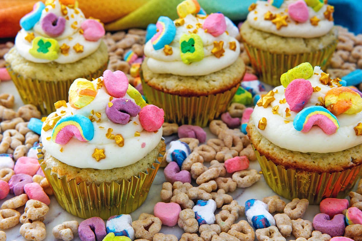 Landscape head-on view of Lucky Charms cupcakes with cereal all around.