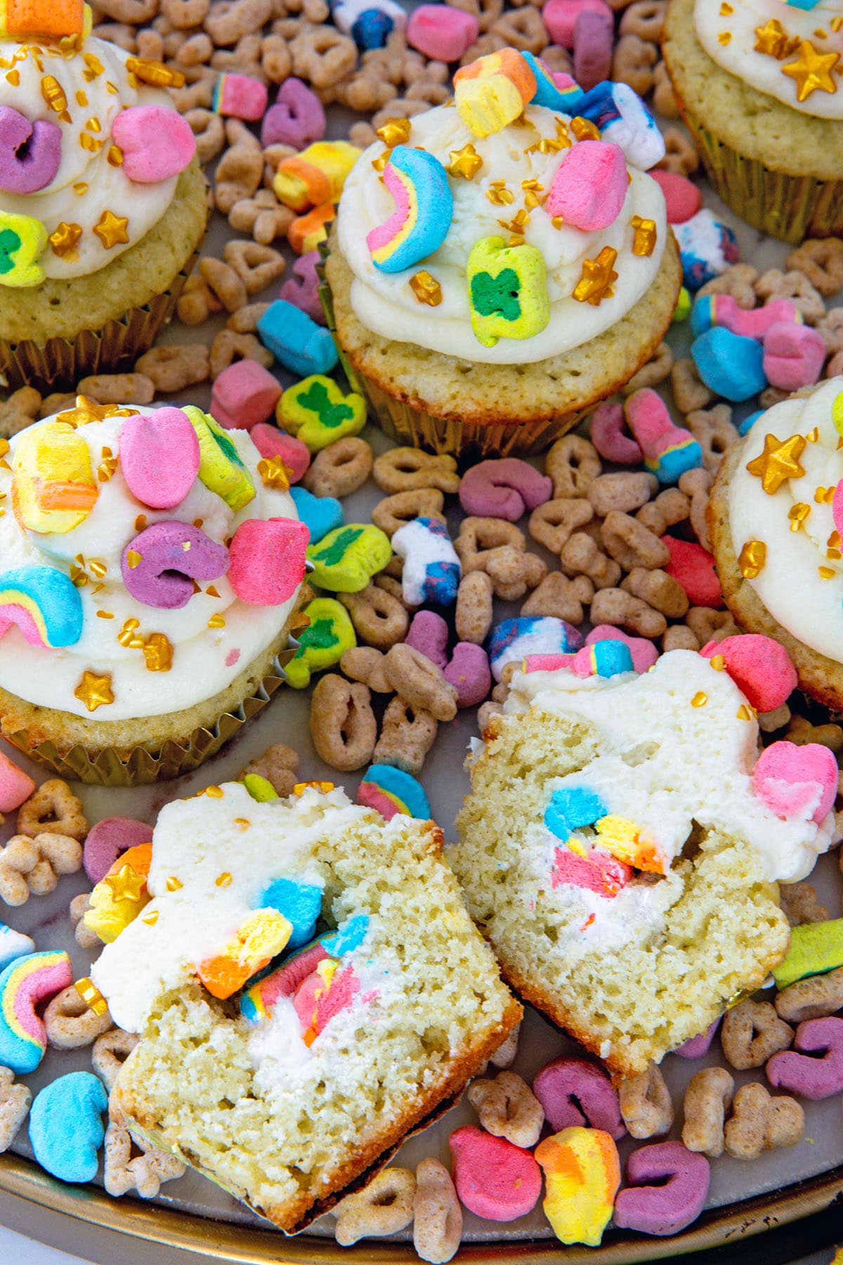 Overhead view of Lucky Charms cupcakes on a platter with one cut in half to show marshmallow cream filling.