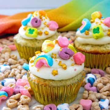 Closeup view of a Lucky Charms cupcake with marshmallow buttercream frosting, gold stars, and cereal marshmallows on top.