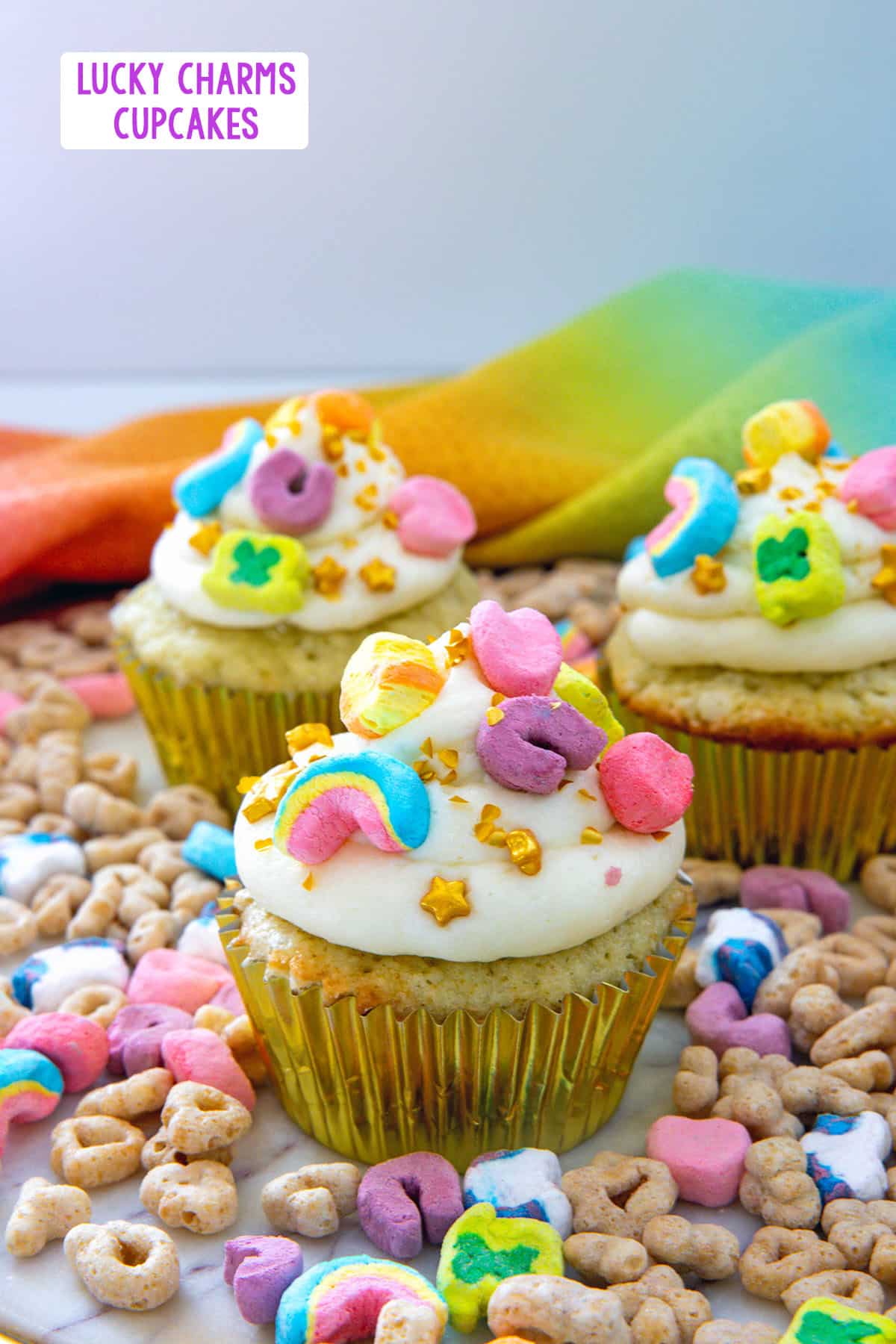 Head-on view of a Lucky Charms cupcake surrounded by cereal and more cupcakes with recipe title at top.