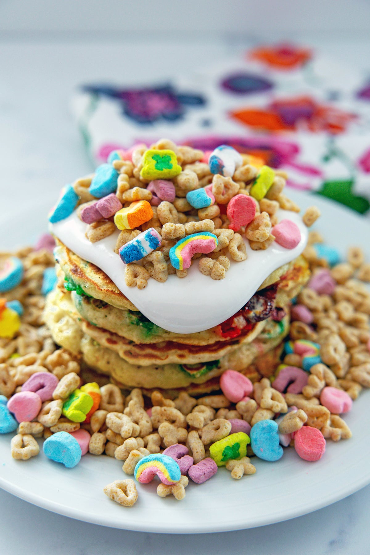 Head-on view of a stack of Lucky Charms pancakes topped with marshmallow sauce and lots of cereal.