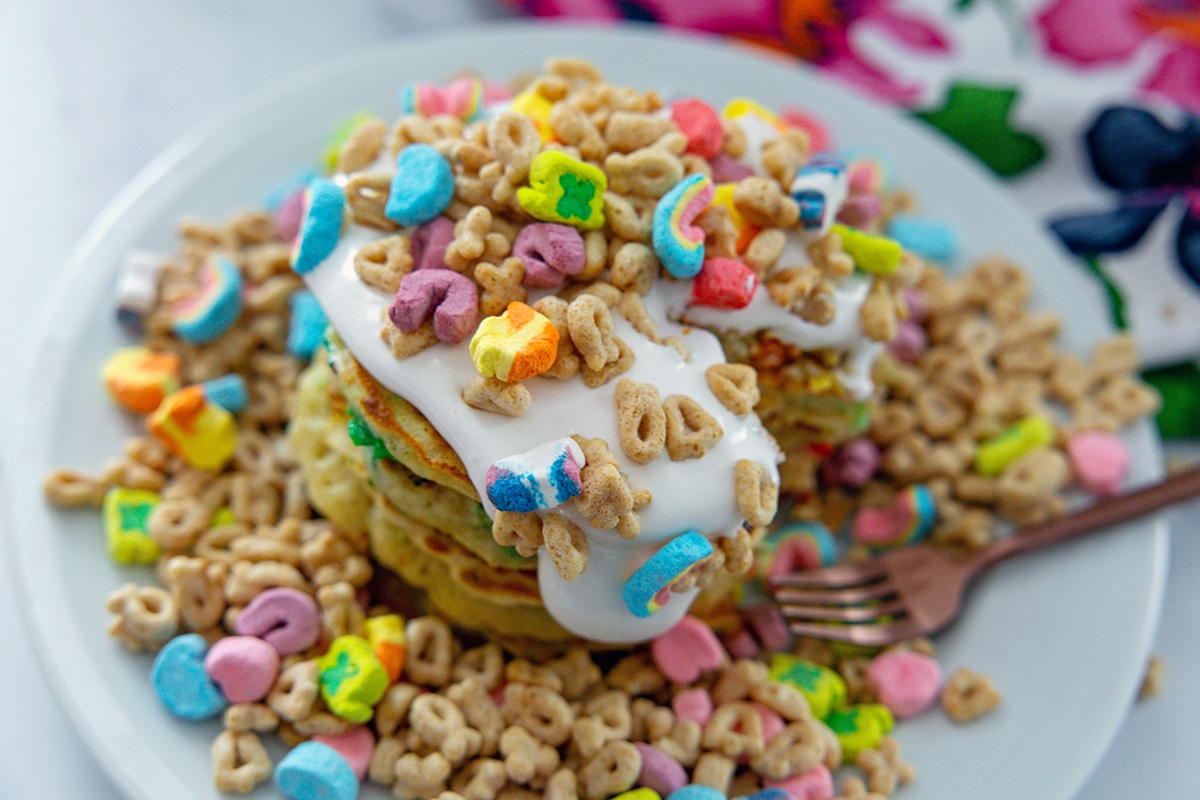 Landscape view of Lucky Charms pancakes with marshmallow sauce on a cereal filled plate.