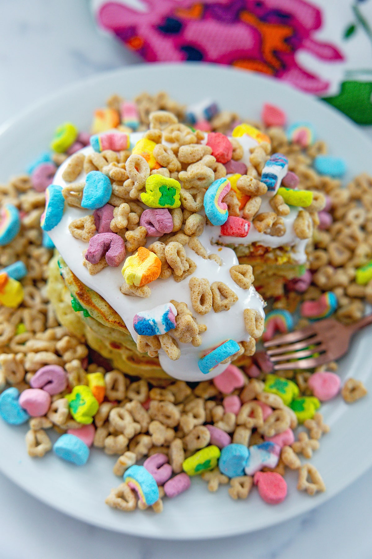 Overhead view of a plate of cereal with a stack of Lucky Charms pancakes with marshmallow sauce.