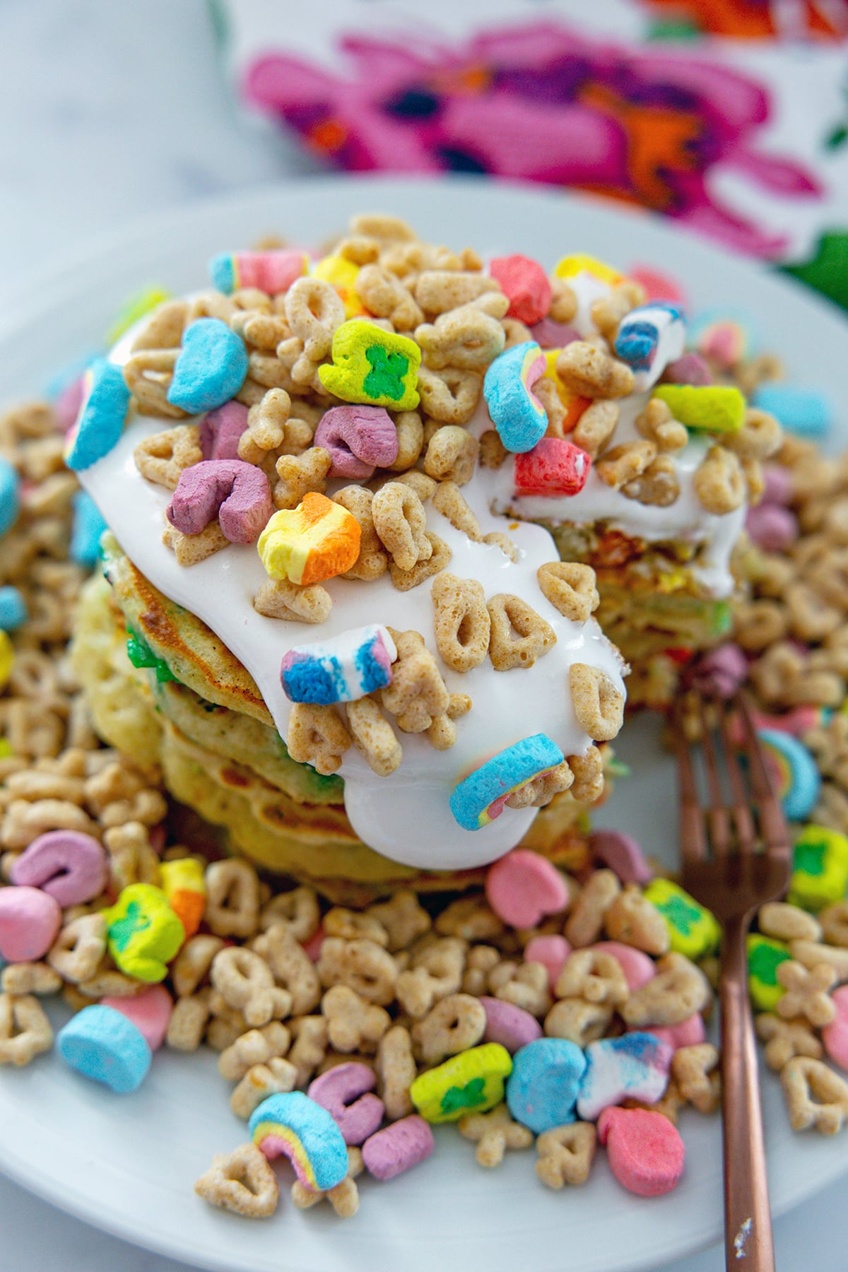 Stack of Lucky Charms pancakes topped with marshmallow sauce and cereal.