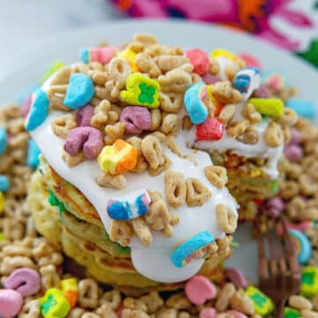 Closeup view of Lucky Charms pancakes with lots of marshmallow sauce and cereal.