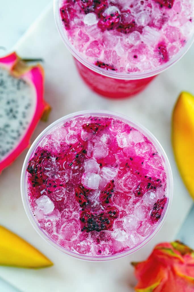Overhead view of two Mango Dragonfruit Refreshers with lots of ice and fruit all around.