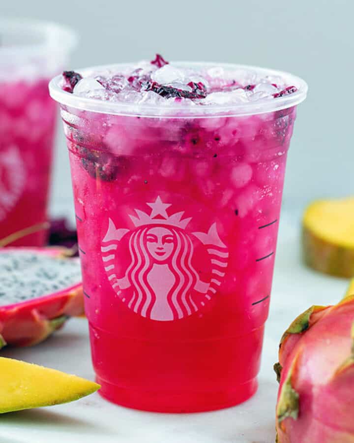 Head-on closeup view of a mango dragonfruit refresher with fresh mango and fresh dragon fruit in background.