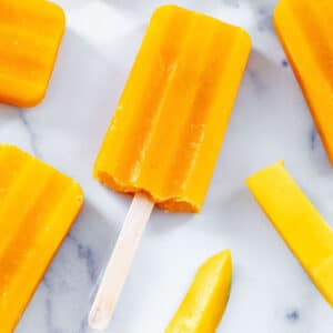 Closeup view of a mango popsicle with sliced mangos all around.