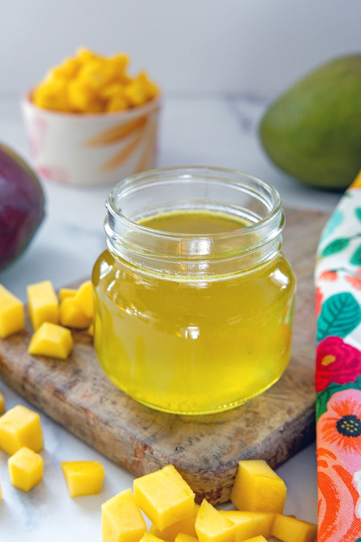 Small jar of yellow mango syrup with chopped mango all around.