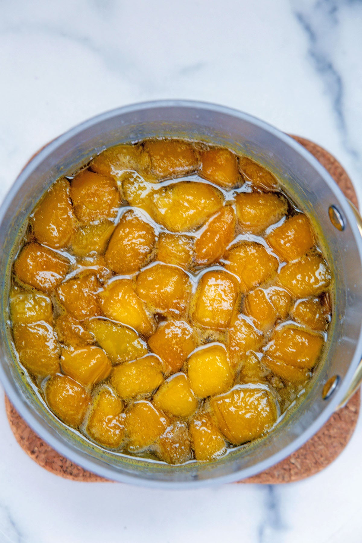 Overhead view of chopped mango simmered with water and sugar in saucepan.