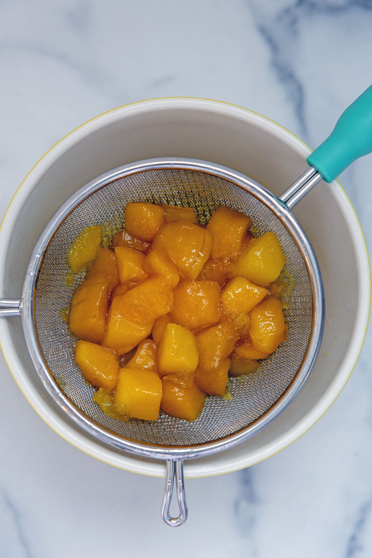 Overhead view of a mesh strainer with simmered mango over a bowl.