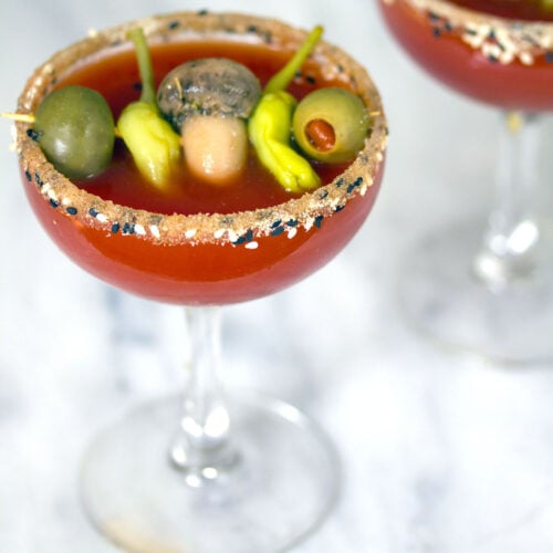 Closeup overhead view of a Manhattan dirty bloody mary in a coup glass with fun garnish.