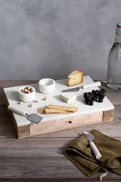 Marble top serving board with cheese and knives.