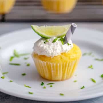 Head-on view of a margarita cupcake with marshmallow frosting, straw, and lime wedge.
