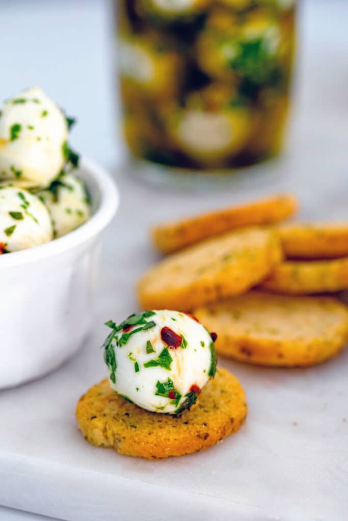 Marinated mozzarella ball on a crostini with more crostini and mozzarella pearls in background.