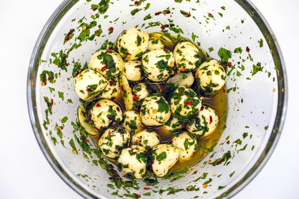 Mozzarella pearls in a mixture of olive oil and herbs in a bowl.