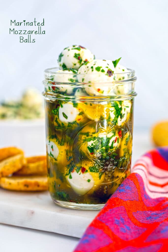 Mozzarella balls in a jar with oil and herbs with crostini in the background and recipe title at top.