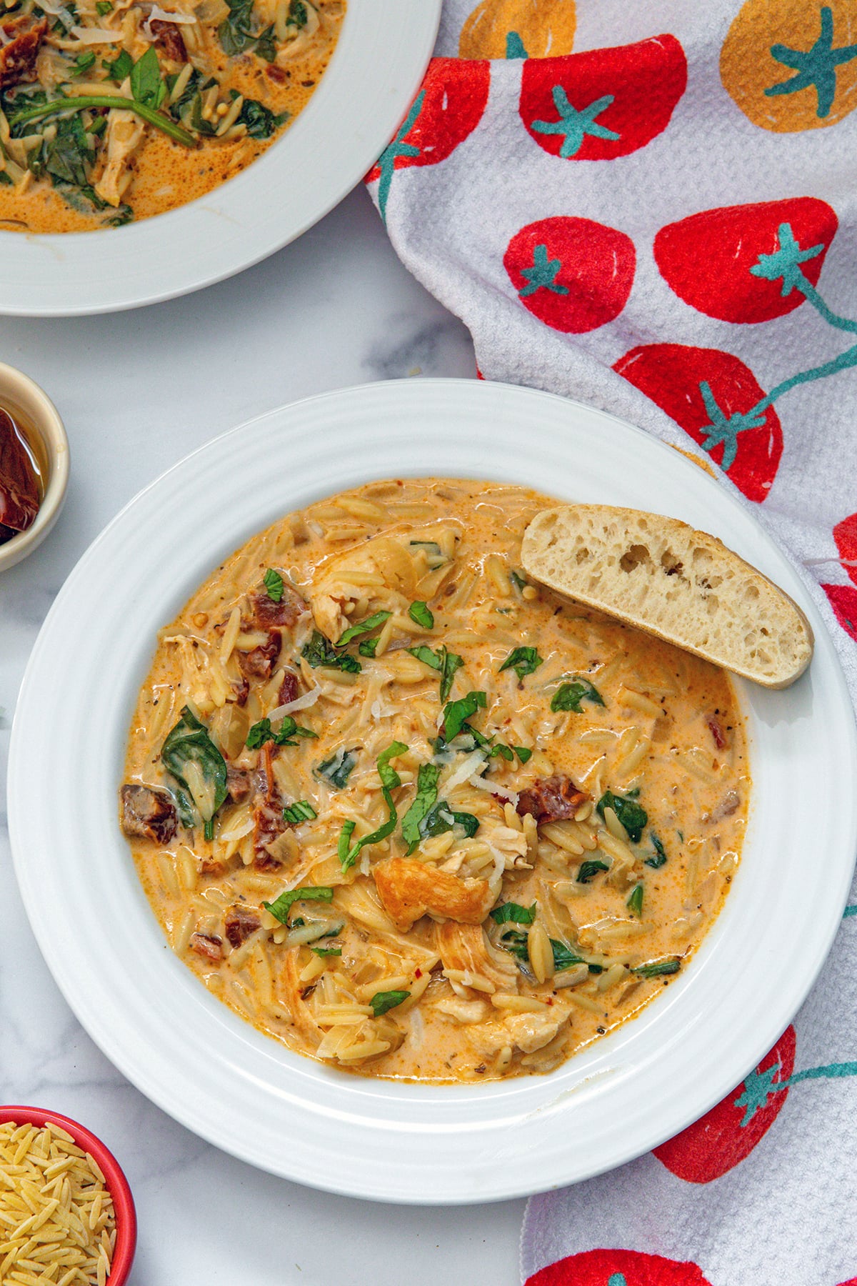 Overhead view of a bowl of marry me chicken soup with orzo, spinach, and sundried tomatoes and bread on side of bowl.