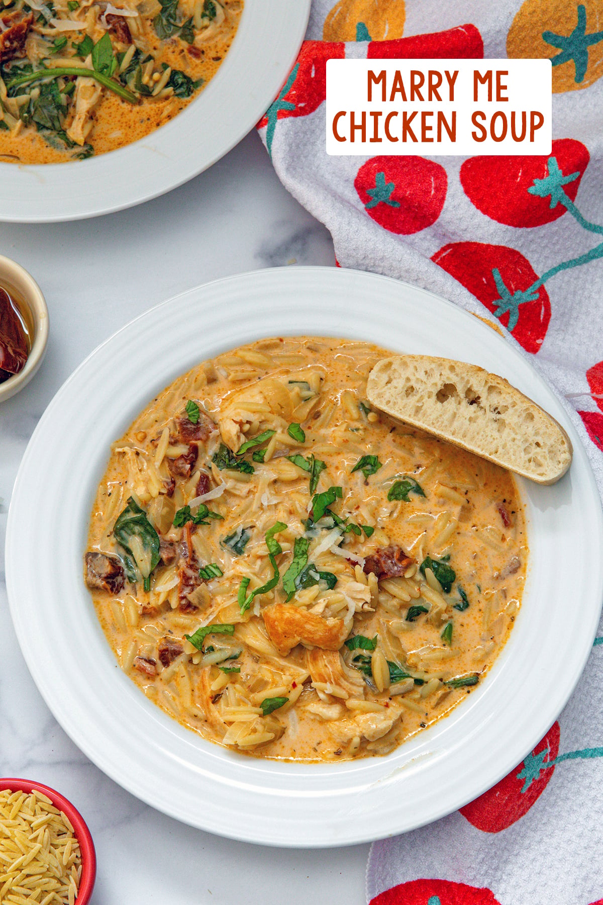 Overhead view of a bowl of marry me chicken soup with orzo, spinach, and sundried tomatoes and bread on side of bowl with recipe title at top.