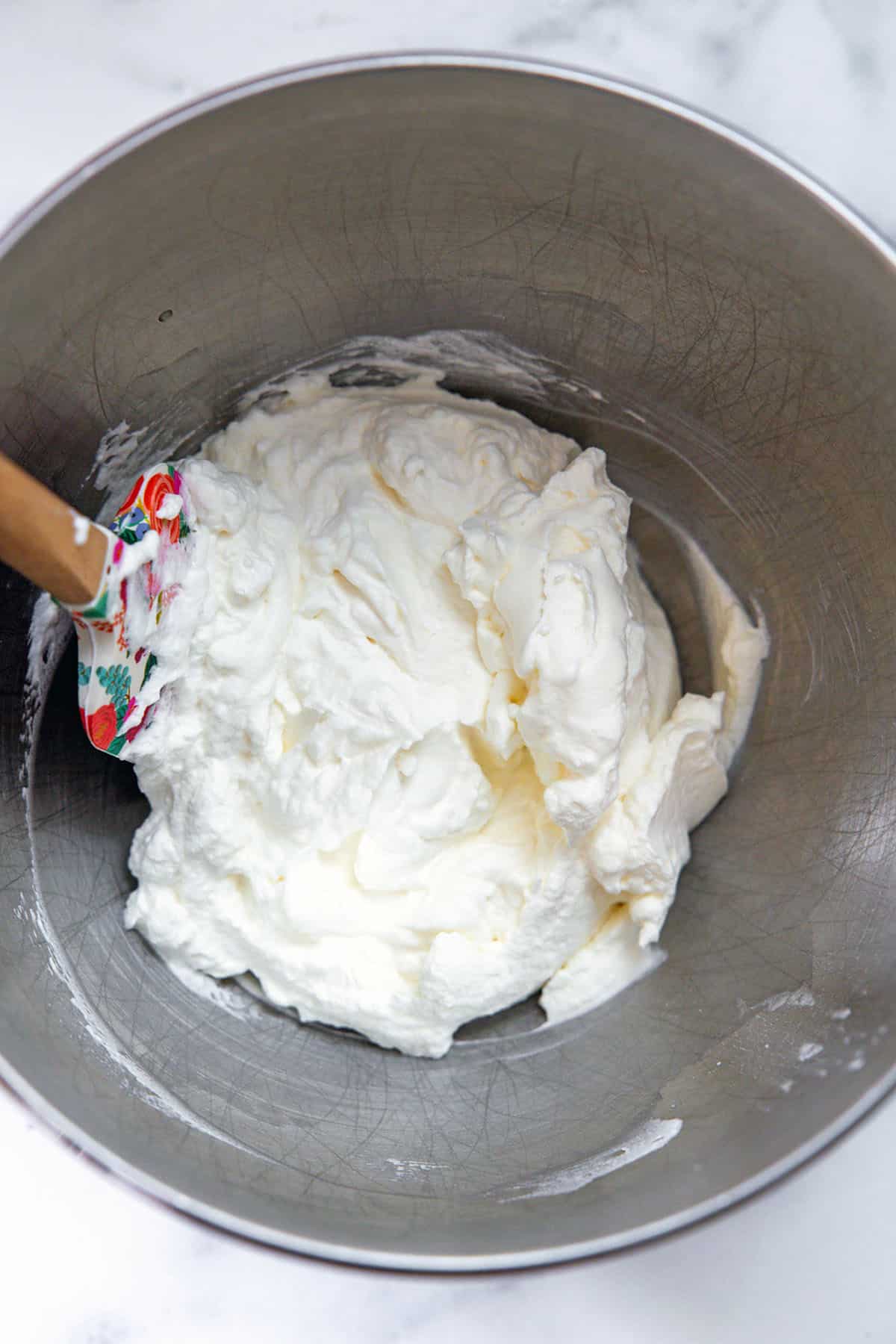 Marshmallow whipped cream in mixing bowl with spatula.