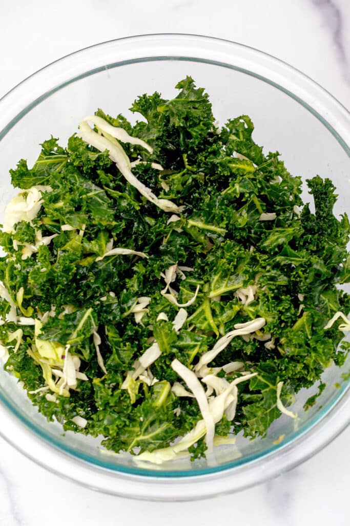 Massaged kale an shredded green cabbage mixed together in bowl.