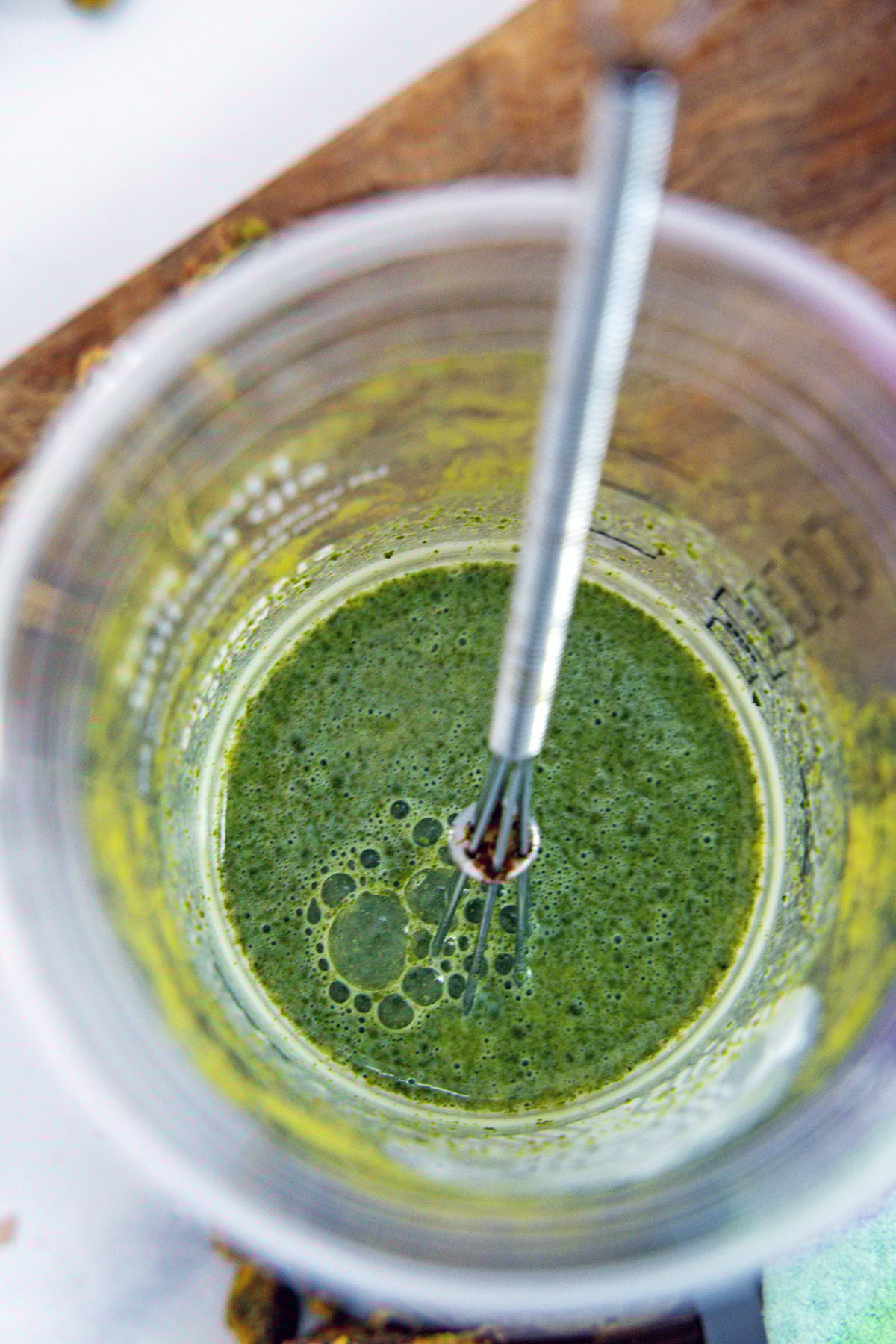 Overhead view of matcha being whisked into milk in cup with tiny whisk.