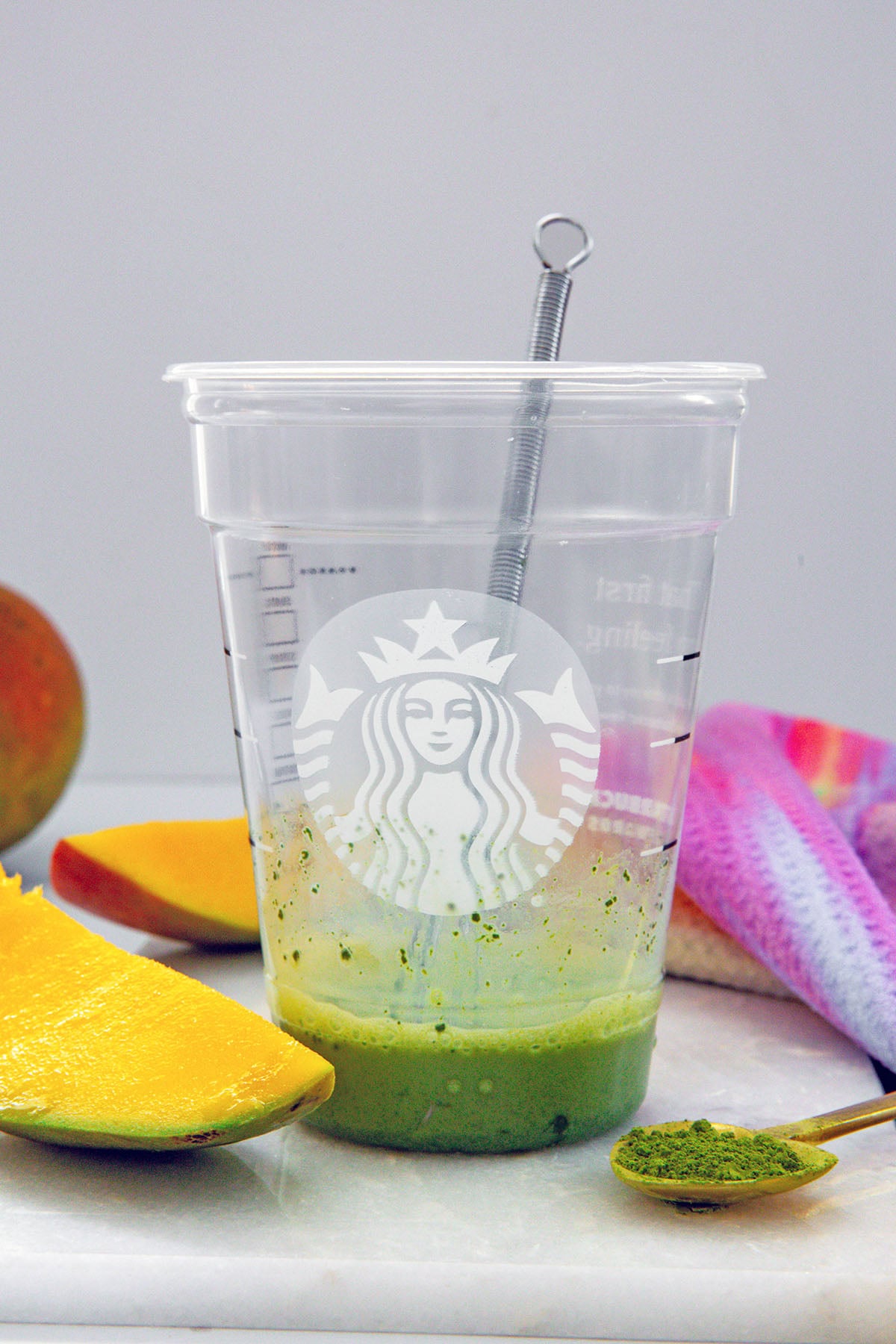 Matcha powder and a little bit of milk on the bottom of a Starbucks cup with tiny whisk.